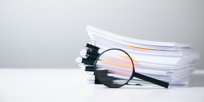 Stack of reports with a magnifying glass